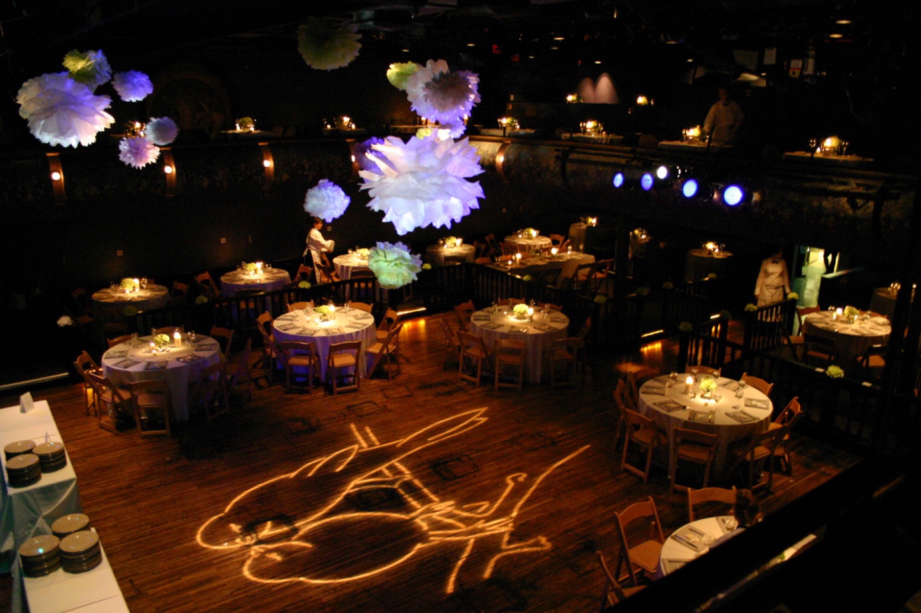 The auditorium floor set for a reception, with paper flowers overhead and a monogram projected on the hardwood